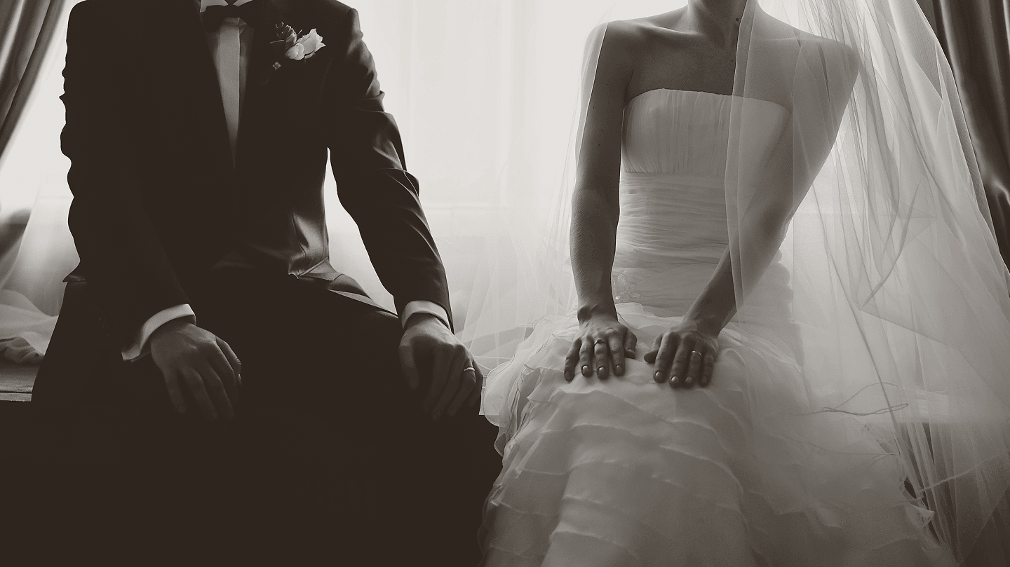 Una novia y un novio sentados lado a lado, en blanco y negro, con las manos sobre el regazo